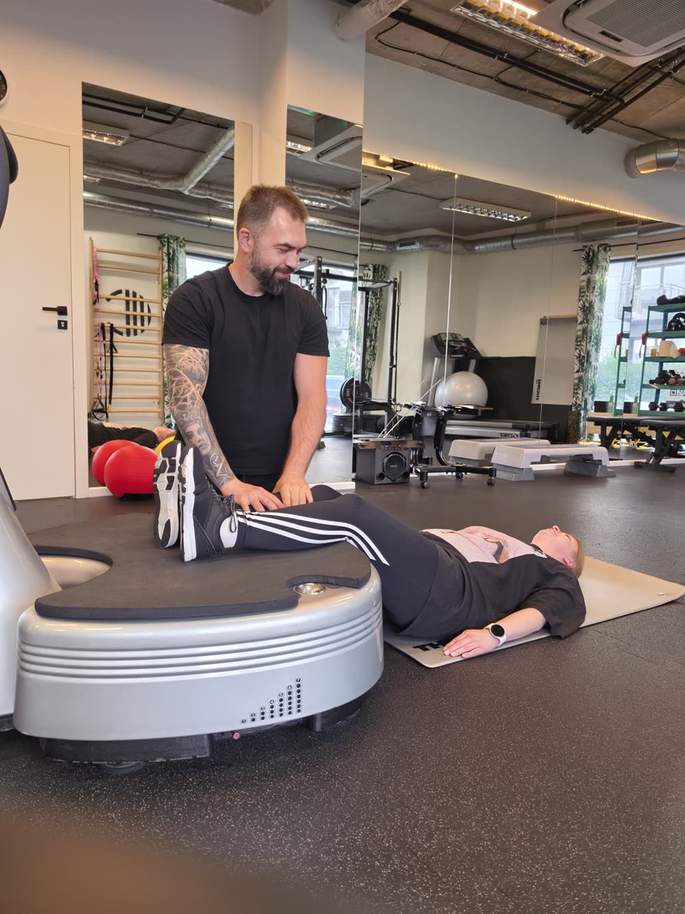 Trener asystuje klientce podczas ćwiczenia regeneracyjnego na Power Plate